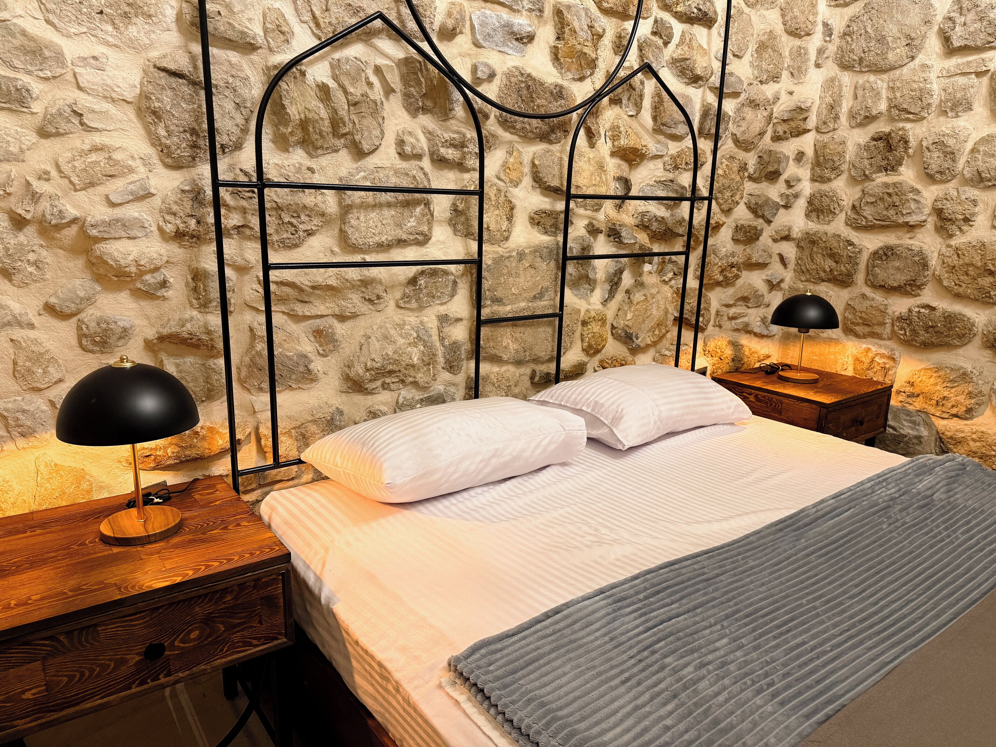 A bed with white bedding, a grey throw, and a black lamp on a wooden nightstand.