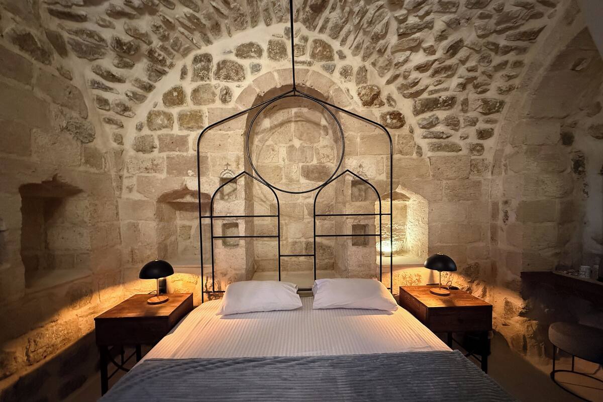 A stone-walled room with a bed, two bedside tables, and a chair.