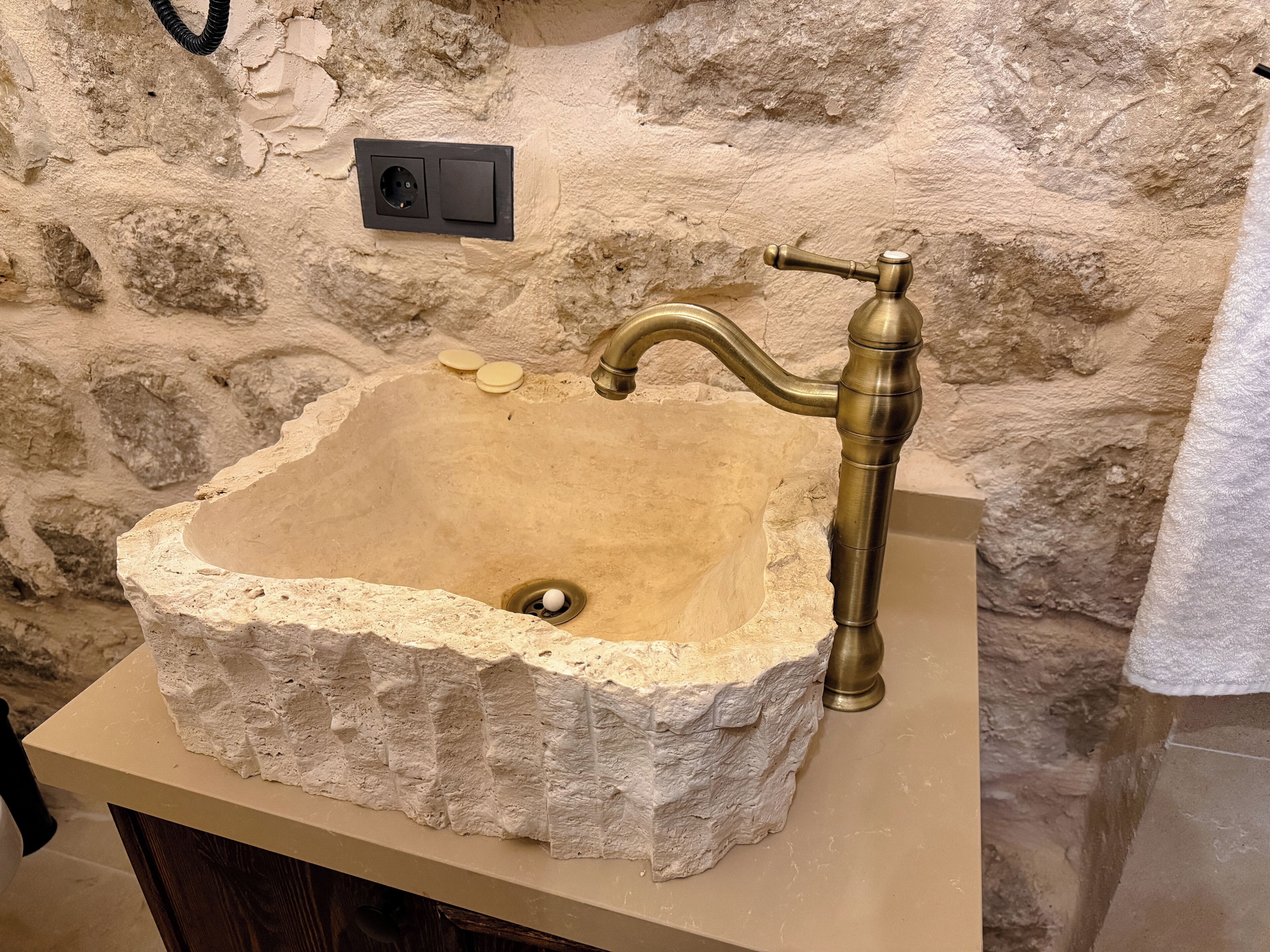 A stone sink with a brass faucet, a power outlet, and a soap dish on a countertop.