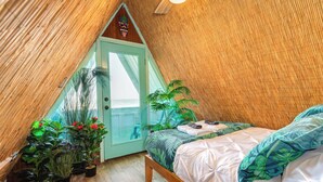 Une pièce triangulaire comprenant un lit, des plantes en pot et une porte donnant sur l’extérieur.