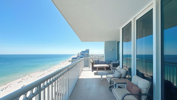 A balcony with a view of the beach and ocean, furnished with chairs and a table.