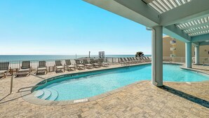 A pool area with lounge chairs, a pool, and a view of the ocean.