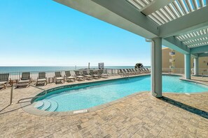 A pool area with lounge chairs, a pool, and a view of the ocean. - The Colonnades 1803 | Walk to HangOut! | Beachfront, Pool, Sauna, Fitness Center | Beach Getaways (Gulf Shores)