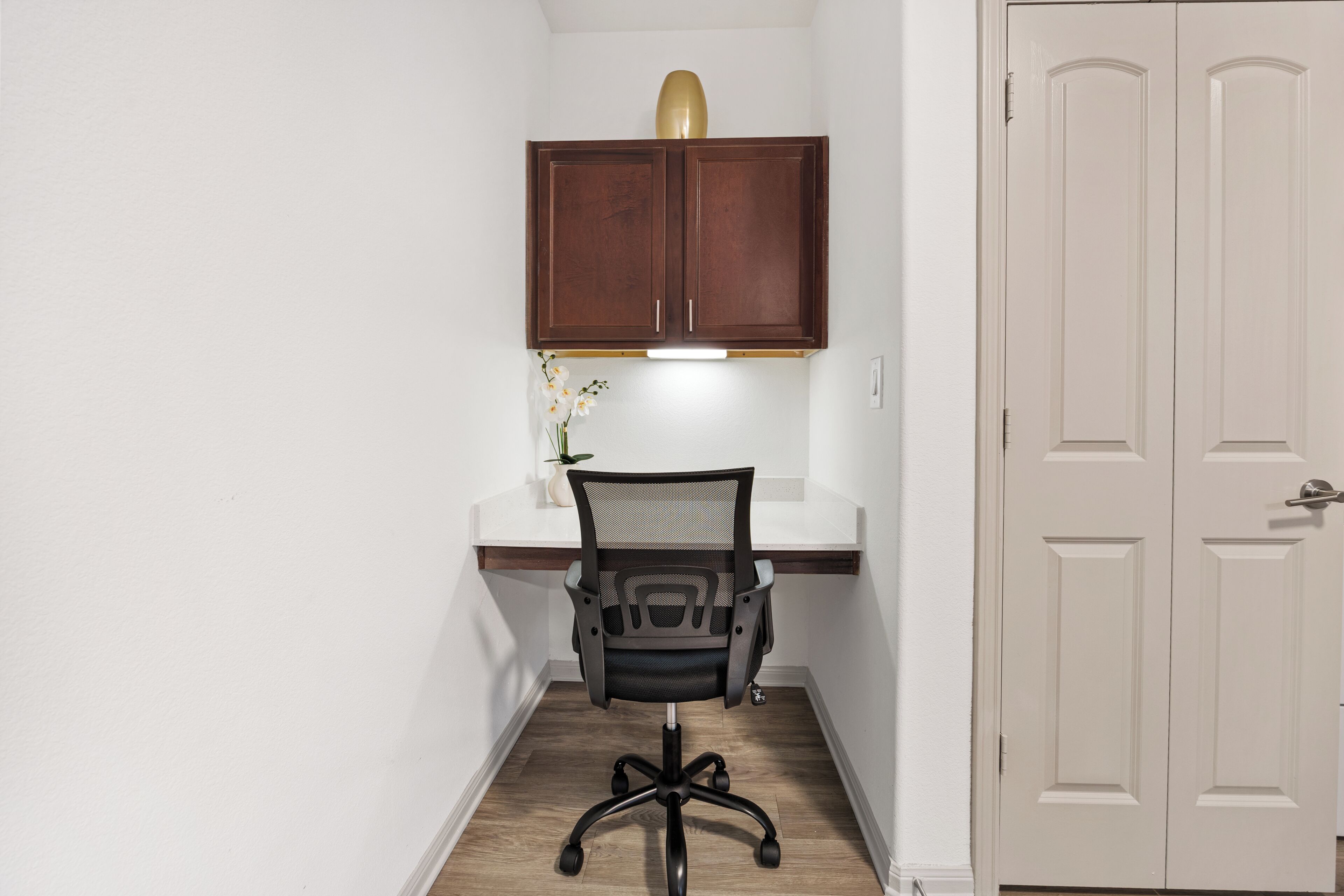 Een kleine kantoorruimte met een bureau, stoel en een kast erboven.