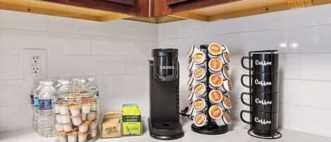 A kitchen counter with a Keurig coffee maker, a coffee mug holder, and jars of water and tea.