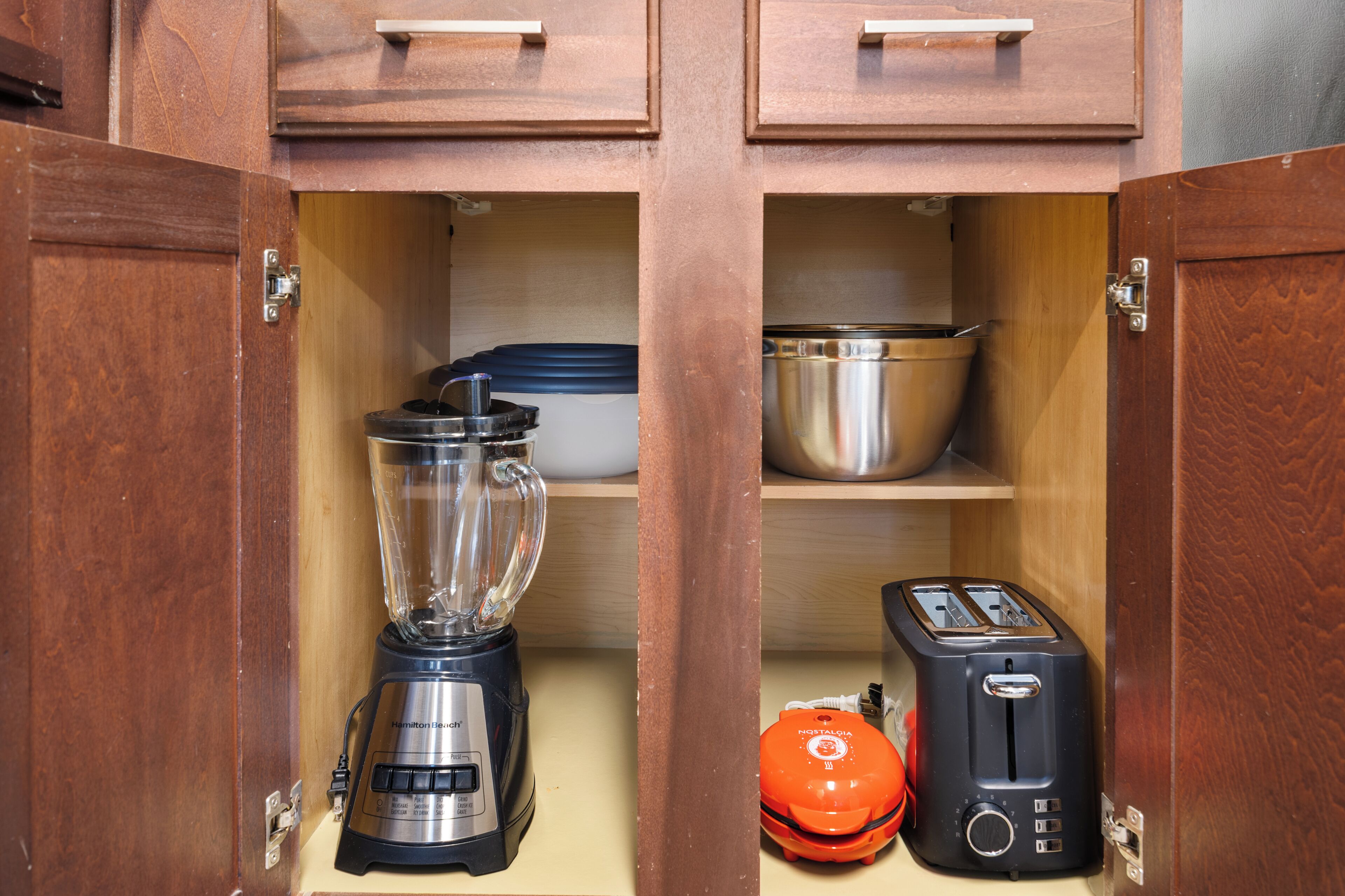Ein Küchenschrank mit Blender, Toaster und einem orangefarbenen Gerät auf den Regalen.