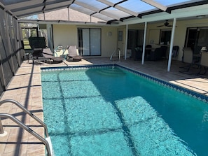 Ein klares Schwimmbecken mit überdachter Terrasse, einer Leiter und Gartenmöbeln.