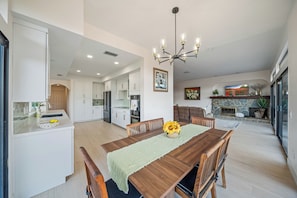A spacious kitchen with white cabinets, a dining area with a wooden table and chairs, and a stone fireplace.