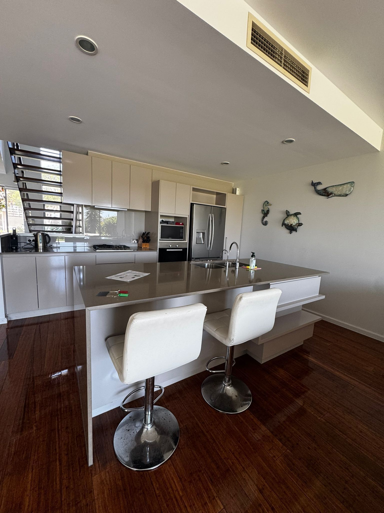 A modern kitchen with a central island, stainless steel appliances, and a seating area with two white chairs.