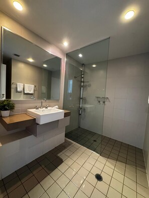 A modern bathroom with a glass-enclosed shower, a white sink with a wooden countertop, and a large mirror. - Fairway Retreat (Magenta)