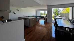Een moderne keuken met een centraal eiland, een eethoek met een grote tafel, en uitzicht op de omgeving door grote ramen.