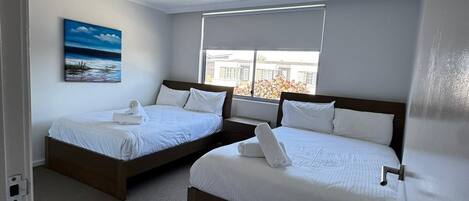 A hotel room with two beds, a painting on the wall, and a window with a view.