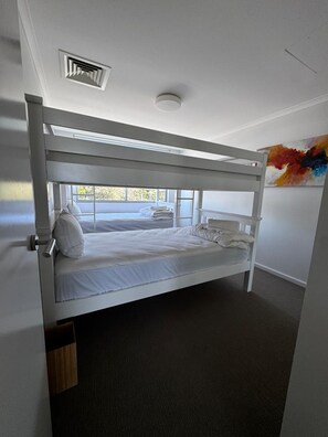 A bunk bed with a window, a ceiling vent, and a partial view of a room with a door and a wall-mounted artwork. - Fairway Retreat (Magenta)