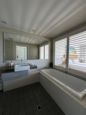 A modern bathroom with a bathtub, a sink, and a large mirror. - Fairway Retreat (Magenta)