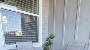 Une table à plateau en verre, quatre chaises, une plante en pot et une fenêtre avec des stores.