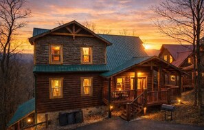 A log cabin with a porch, multiple windows, and a stone foundation. - NEW! Pool! Ultra Luxe 4BR Cabin w/Theater (Gatlinburg)