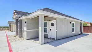A single-story building with a flat roof, a covered porch, and a garage door. - Welcoming 2-bedroom house with AC in charming Eagle Pass (Eagle Pass)