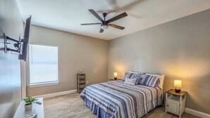A bedroom with a bed, nightstands, a ceiling fan, a window, and a desk with a plant. - Welcoming 2-bedroom house with AC in charming Eagle Pass (Eagle Pass)