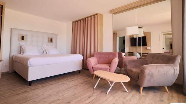 Une chambre d’hôtel avec un lit, deux fauteuils, une petite table et un grand miroir.