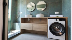Une salle de bain moderne avec une douche à l’italienne en verre, deux vasques, un lave-linge et un meuble-lavabo en bois.