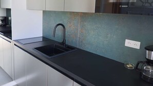 Une cuisine moderne avec un plan de travail noir, des armoires en acier inoxydable et un appareil électroménager de la marque Bosch.