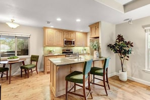 Una cocina con armarios de madera, microondas, estufa y comedor con mesa y sillas.