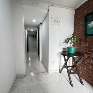 A hallway with a tiled floor, a potted plant on a table, and a brick wall with a framed picture.