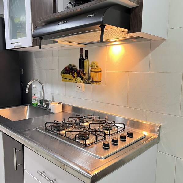 A kitchen with a gas stove, stainless steel countertops, a built-in oven, and a wine rack with bottles and grapes.