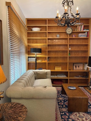 A living room with a sectional sofa, a wooden bookshelf, a chandelier, and a patterned rug.