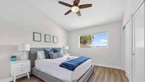 A bedroom with a bed, nightstand, lamp, ceiling fan, window, and a view of the outdoors. - Hot Tub & Canyon Views! | 10 Min to La Jolla Beach (San Diego)