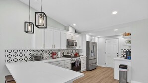 A modern kitchen with white cabinetry, a central island, stainless steel appliances, and pendant lighting. - Hot Tub & Canyon Views! | 10 Min to La Jolla Beach (San Diego)