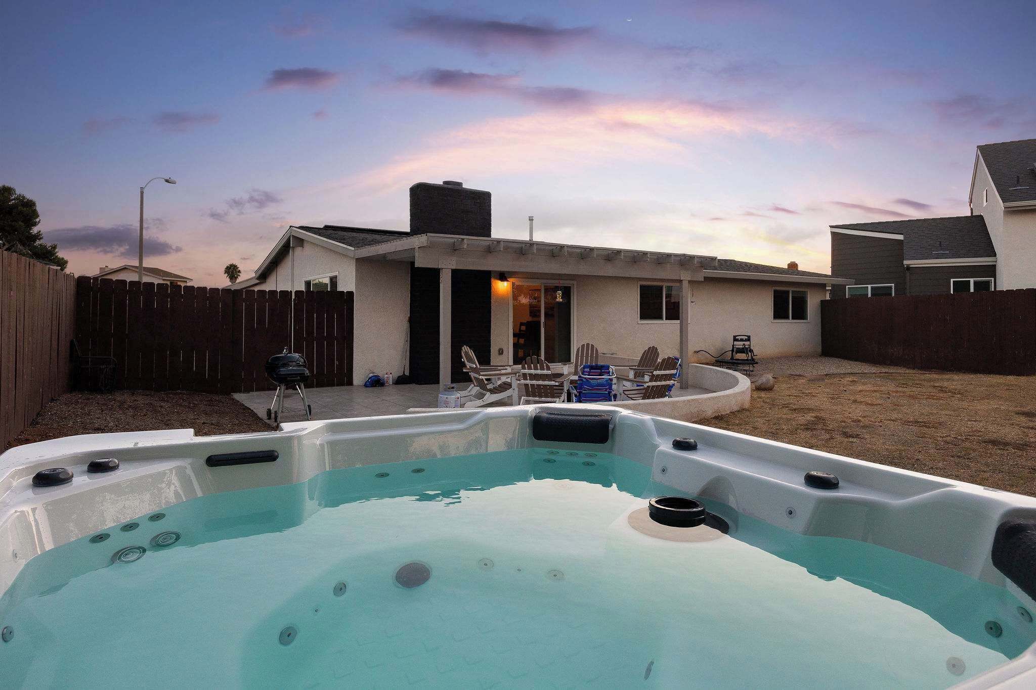 A backyard with a hot tub, a barbecue grill, and a patio with chairs.