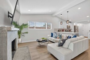 Ein modernes Wohnzimmer mit Kamin, einer Couch, einem Couchtisch und einer Küche im Hintergrund.