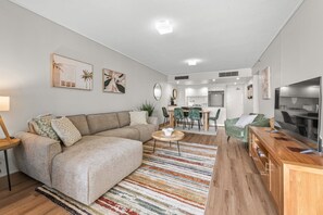 A modern living room with a sectional sofa, a dining area, and a kitchen in the background. - Luxe 3BR Apt w/ River Views + Resort Amenitie (Brisbane)