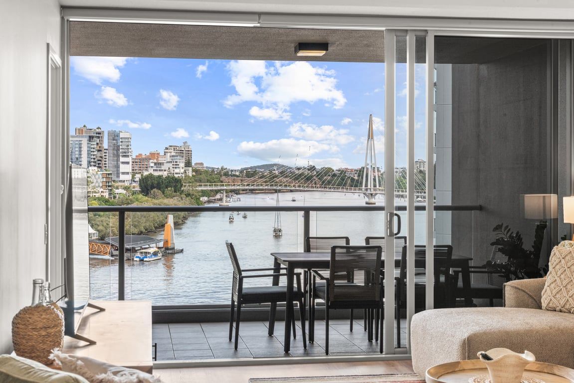 A balcony with a view of a river, a bridge, and buildings in the distance.