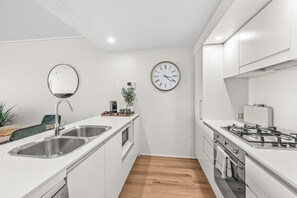 Eine moderne Küche mit weißen Schränken, Edelstahlgeräten, einer runden Wanduhr und Holzboden.