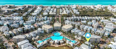 An aerial view of a coastal residential area with a central swimming pool surrounded by houses.