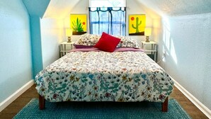 A bedroom with a sloped ceiling, a bed with floral bedding, a red pillow, two bedside tables with lamps, and artwork on the walls. - Wonderful 2-bedroom house in Denver perfect for your getaway (Denver)