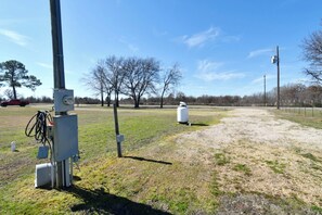A grassy field with utility poles and equipment, a red truck in the distance, and leafless trees. - RV SPACE FOR RENT (Alba)