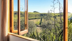 A window with a view of a green landscape, including fields and trees. - The Loft at Cypress Ridge Estate (Waiheke Island)