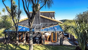 A wooden house with a glass extension, surrounded by trees and a hill. - The Loft at Cypress Ridge Estate (Waiheke Island)
