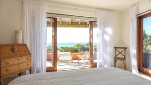 Ein Schlafzimmer mit einem Bett, einer Holzkommode und Meerblick durch eine Glastür.