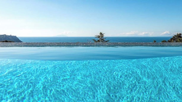 Ein Pool ohne Ende mit klarem, blauem Wasser, Blick auf den Ozean und eine entfernte Bergkette.