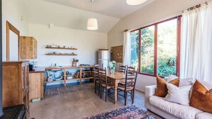 Una cocina acogedora con armarios de madera, una mesa de comedor y sillas. Hay un ventanal con cortinas, un sofá con cojines y una alfombra en el suelo.