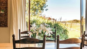 Una mesa de comedor con sillas de madera, un jarrón con flores blancas y vistas a vegetación y una valla afuera.