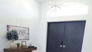 Ein Zimmer mit einer dunklen T ür, einem Holztisch mit einer Vase und einem Schild, sowie einem grauen Teppich auf Holzboden.