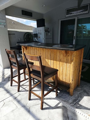 An outdoor kitchen area with a wooden bar and two chairs. - Sioux-Per-Tipsy: Pet-Friendly, Private Pool, Group Travel (Cape Coral)