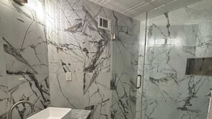 Ein Badezimmer mit Marmorwand, Waschbecken, Toilette und Duschbereich.