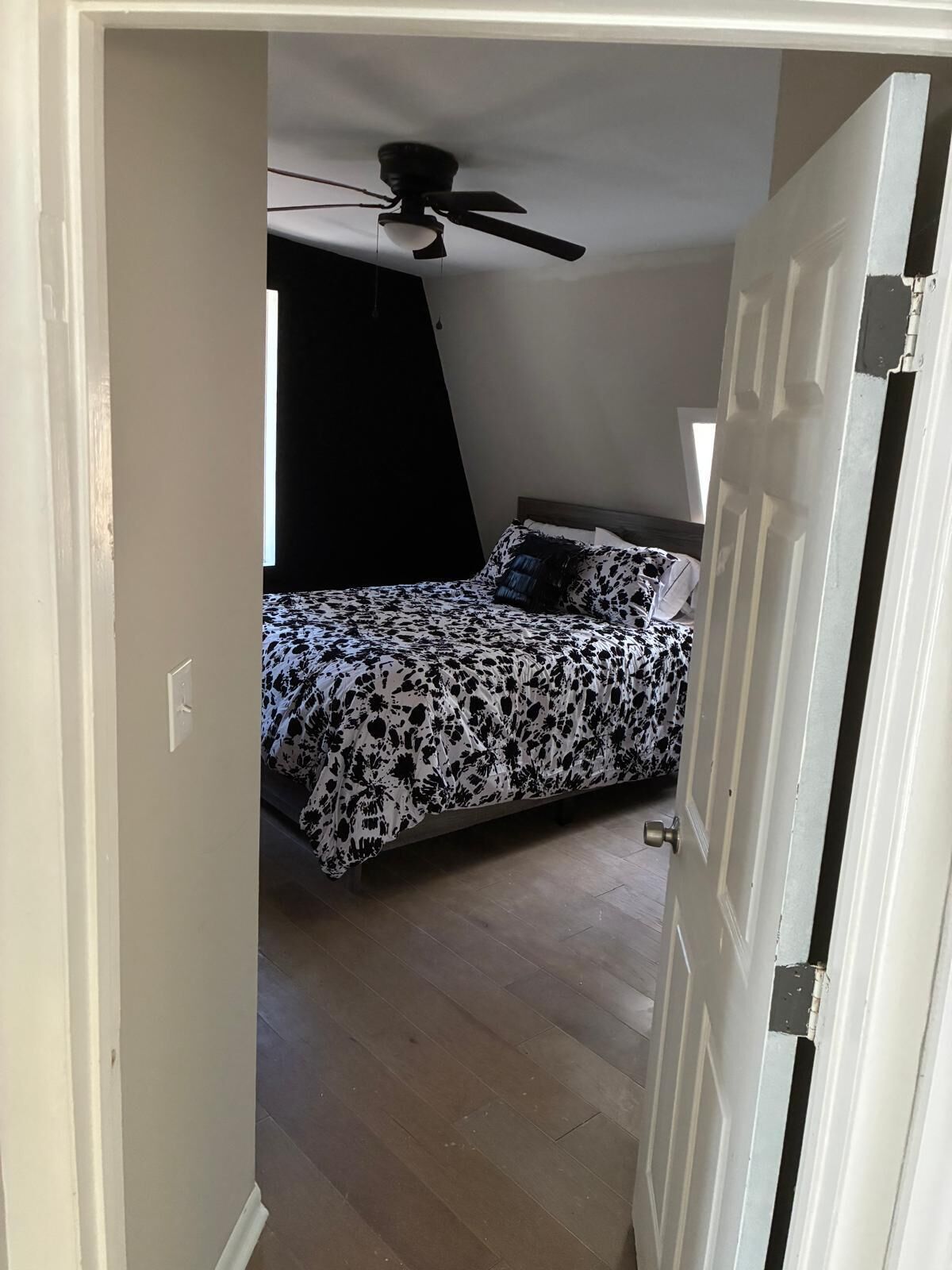 Un dormitorio con ventilador de techo, cama con colcha estampada y puerta que da a otra habitación.