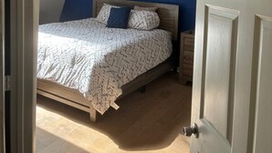 Ein Schlafzimmer mit Bett, Nachttisch, Holz-Kopfteil, einer Tür und einer Deckenleuchte.